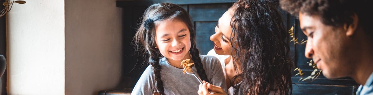 a family eating dinner, focusing on the mother feeding her child with a fork.