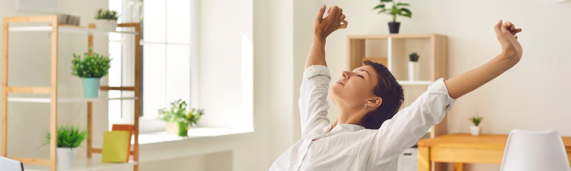 A lady with her arms stretched above her head leaning back on a chair with her eyes closed.