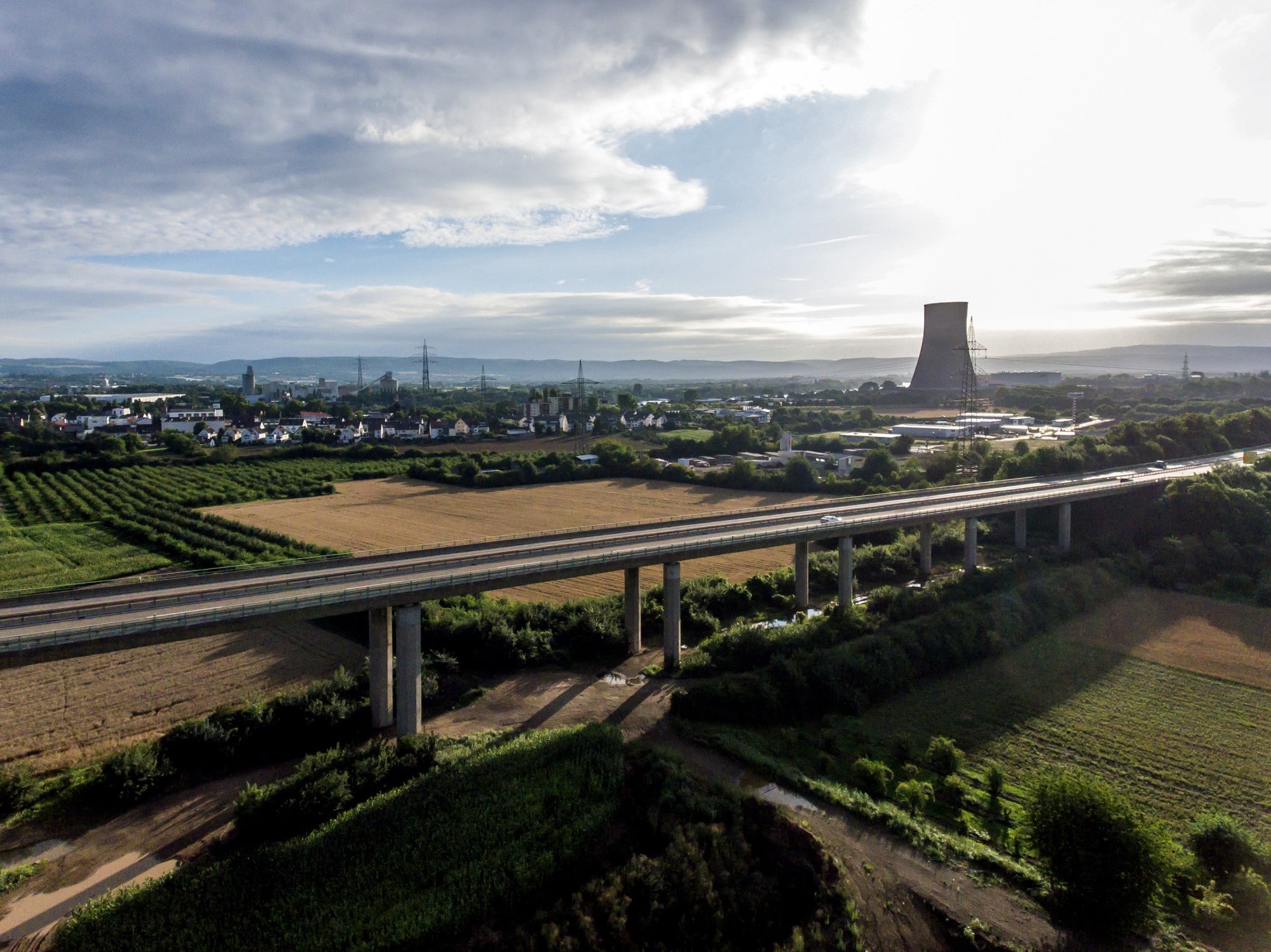 Aerial view of farmland and a road bridge with a nuclear power station and cooling tower in the distance.