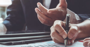 Close‑up of hands holding a pen and discussing printed documents across a desk during a meeting.