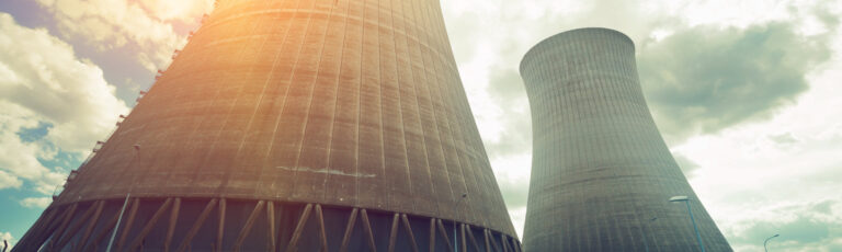 Two large cooling towers rising against a cloudy sky at an industrial power station site.
