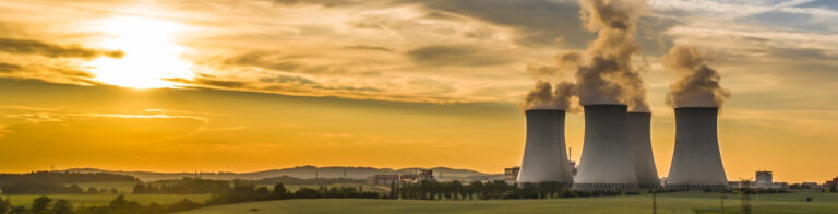 Nuclear power station with four cooling towers releasing steam across green fields at sunset.