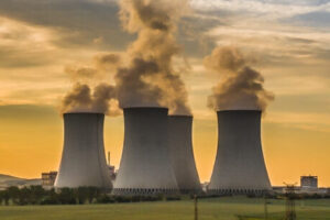 Nuclear power station with four cooling towers releasing steam across green fields at sunset.