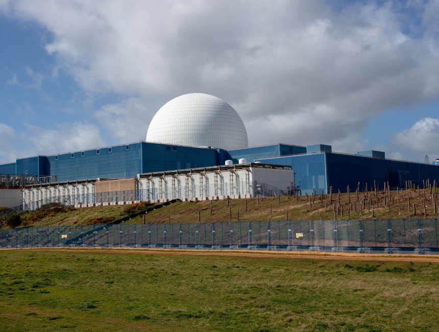 Nuclear power station with domed reactor building and blue industrial structures behind security fencing.