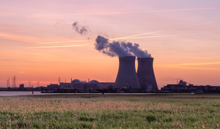 Nuclear power station with two cooling towers emitting steam across fields at sunset.