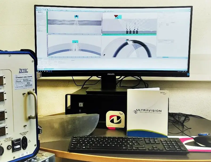 Computer workstation showing pipeline inspection software beside testing equipment and keyboard.